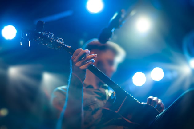 Photograph of a guitarist performing on a stage under blue toned stage lights.