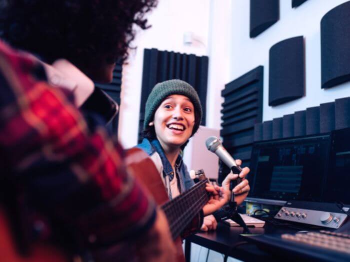 Two musicians in a studio with a guitar and microphone songwriting.