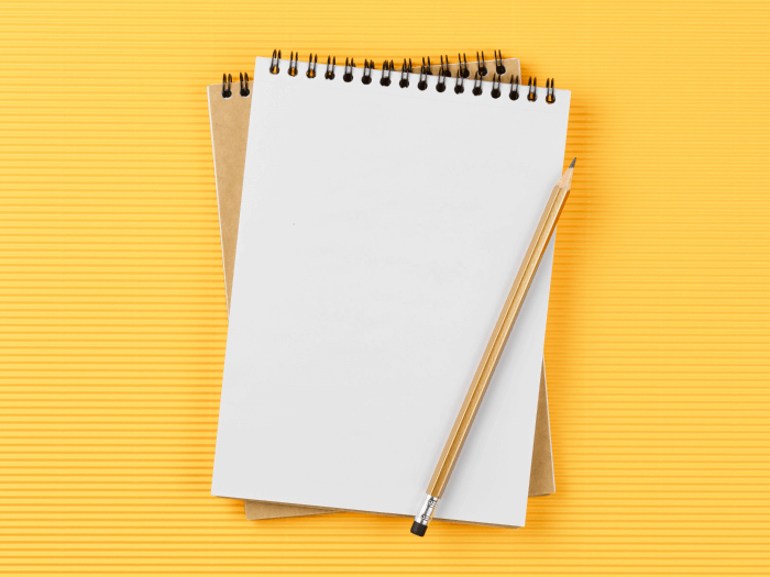 A gold pencil lies across an open notebook, the page is blank and very bright white and the background is a stylised yellow.