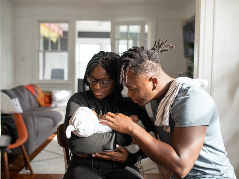 Black mother and father embracing a new born baby, looking down smiling