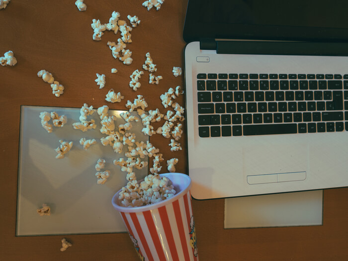 A spilled cardboard cup of popcorn lies next to a laptop computer.