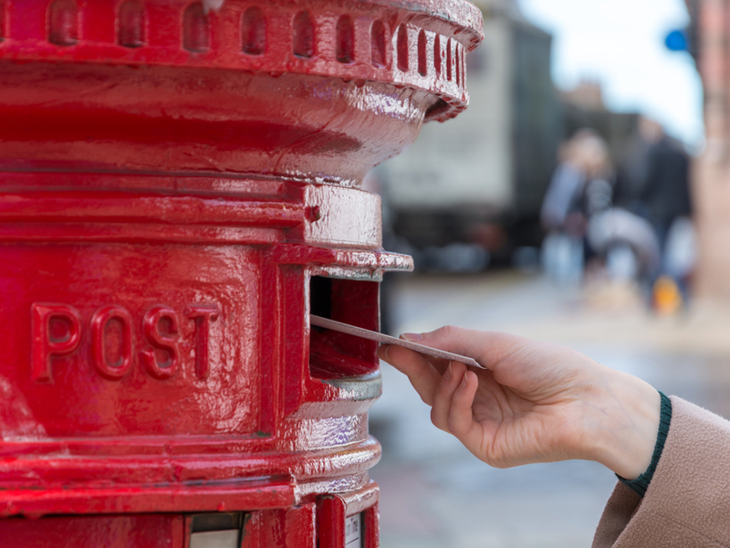 A hand is posting something into a red postbox