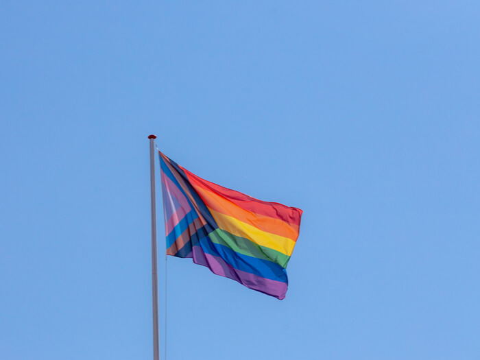 The pride flag flies against a clear bright blue sky