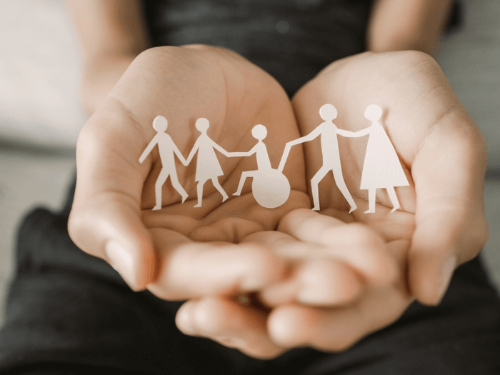 A pair of hands holding paper cut outs of human figures.