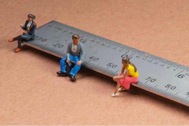 Miniature figures sit on a ruler demonstrating the concept of social distancing to avoid transmission of the coronavirus