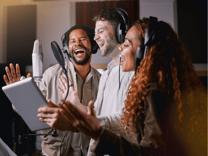 Three vocalists in a recording studio singing into a microphone.