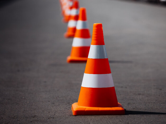 Bright orange and white traffic cones stand in a line on a concrete road
