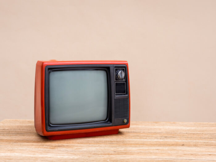 A small red vintage style television on a light wood surface with a pale beige painted background