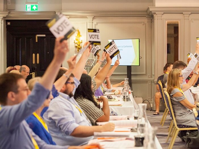 People placing their vote at the MU Delegate Conference 2019, with cards held over head.