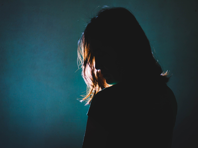 Silhouette of a  person standing against a stage light, the light is shining through their shoulder length hair.