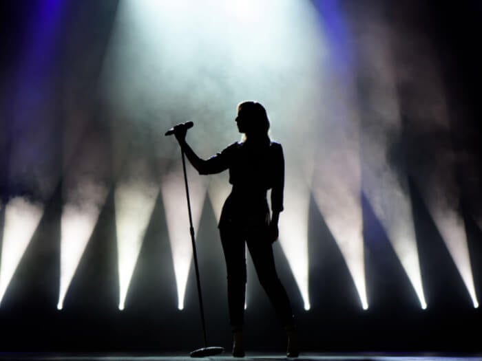 Silhouette of a woman standing on a stage leaning on a microphone