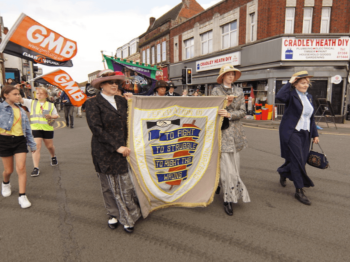 Women trade unionists and activists holding banners and flags as they parade down the street.