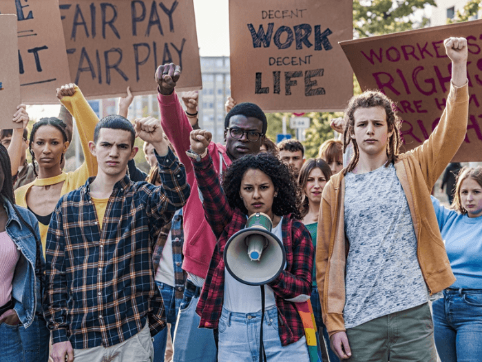 A group of young workers raising their fists in solidarity on a march and holding signs for fair work.